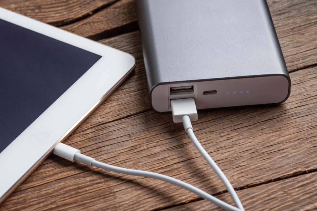 Smartphone charging with power bank on wood board.