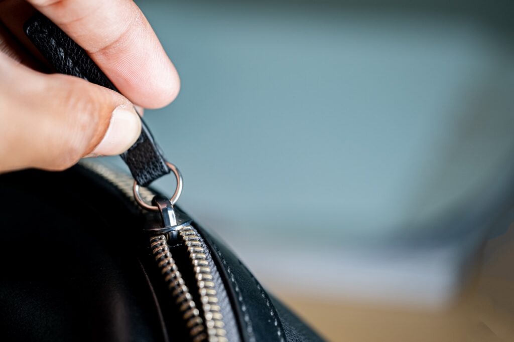 Close-up of a hand holding a zipper pull on a black leather bag.