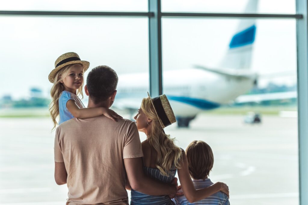 Travel Sentry | ¿A qué hora deberías llegar al aeropuerto? Vista de espaldas de una familia mirando juntos por la ventana en 2026